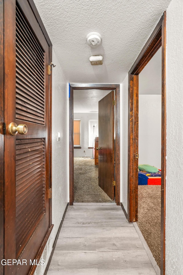 corridor with light wood-style flooring, light carpet, a textured wall, and a textured ceiling