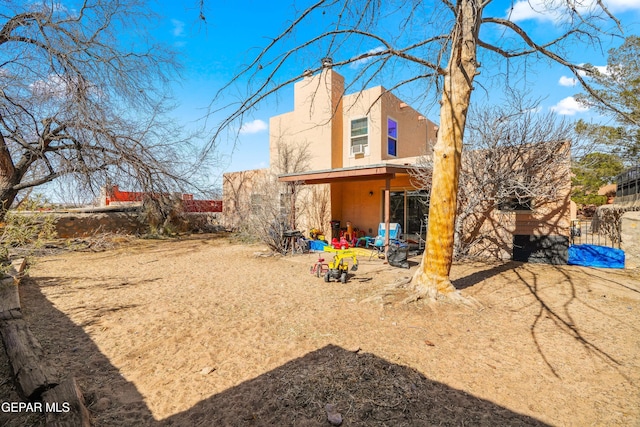 back of house with a chimney, fence, and stucco siding