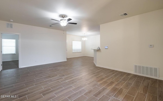 empty room with ceiling fan with notable chandelier, visible vents, and wood tiled floor