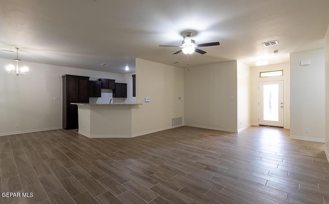 unfurnished living room with ceiling fan with notable chandelier, dark wood finished floors, visible vents, and baseboards