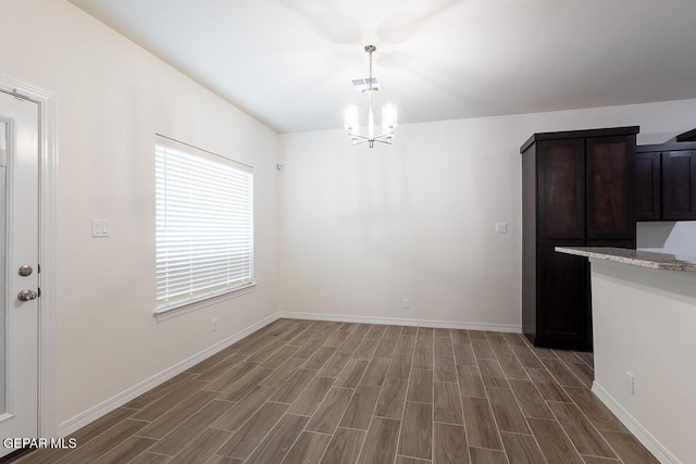 unfurnished dining area featuring wood finish floors, visible vents, baseboards, and an inviting chandelier