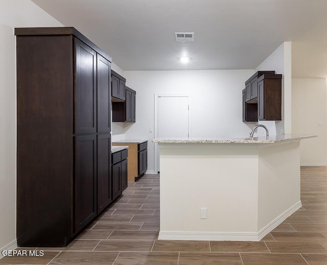 kitchen featuring wood finish floors, visible vents, a peninsula, and light stone countertops