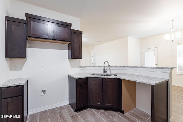 kitchen featuring a peninsula, light stone countertops, dark brown cabinets, and a sink