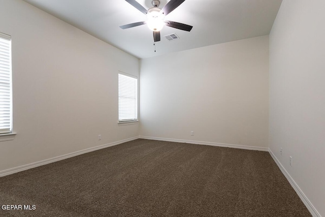 empty room featuring ceiling fan, dark colored carpet, visible vents, and baseboards