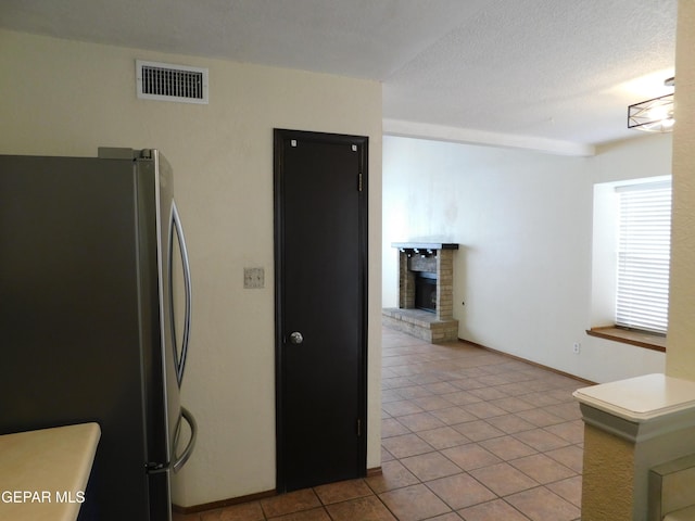 kitchen with a fireplace, light tile patterned floors, visible vents, freestanding refrigerator, and a textured ceiling