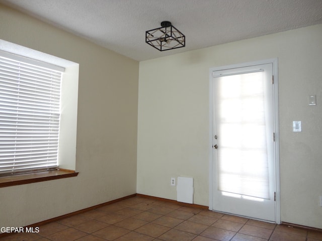 interior space featuring a healthy amount of sunlight, a textured ceiling, baseboards, and light tile patterned floors