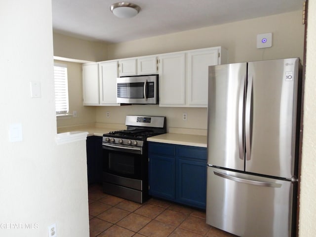 kitchen featuring white cabinets, stainless steel appliances, light countertops, blue cabinetry, and dark tile patterned floors