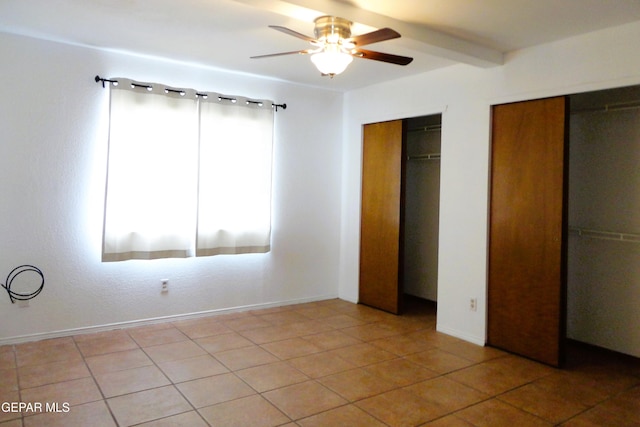 unfurnished bedroom with tile patterned floors, baseboards, two closets, and beamed ceiling