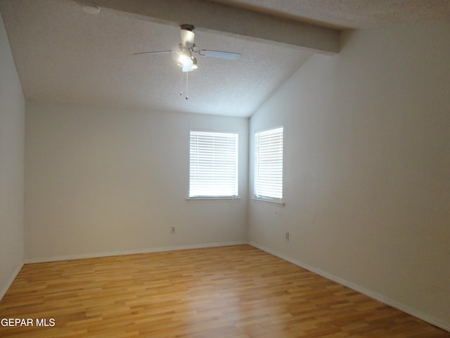 empty room with vaulted ceiling with beams, light wood-style floors, a ceiling fan, a textured ceiling, and baseboards