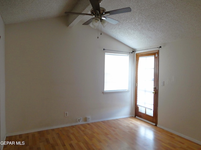 spare room featuring a textured ceiling, light wood finished floors, lofted ceiling, and baseboards