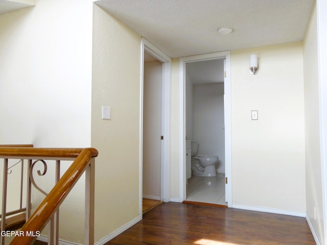 hallway with baseboards, dark wood finished floors, a textured ceiling, and an upstairs landing