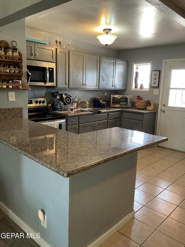 kitchen featuring appliances with stainless steel finishes, stone countertops, light tile patterned flooring, a sink, and a peninsula