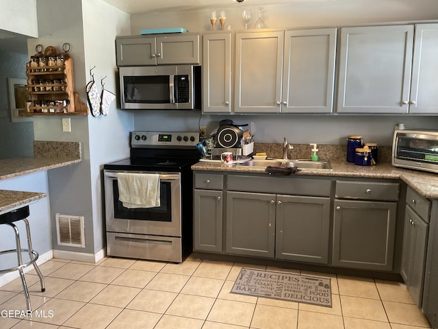 kitchen with light tile patterned floors, gray cabinetry, a sink, visible vents, and appliances with stainless steel finishes