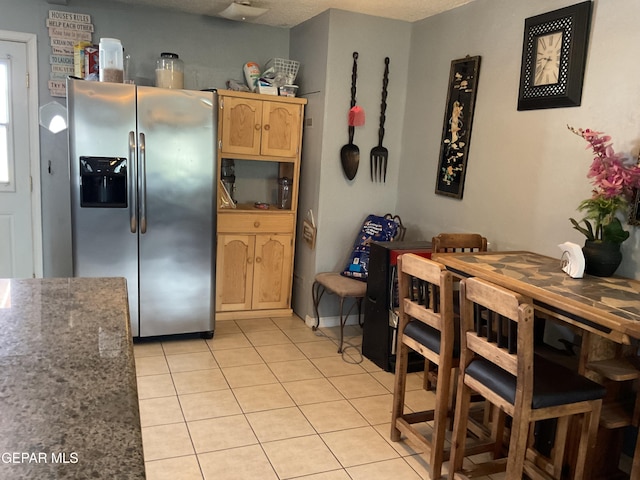 kitchen with stainless steel fridge, dark countertops, a textured ceiling, light brown cabinets, and light tile patterned flooring