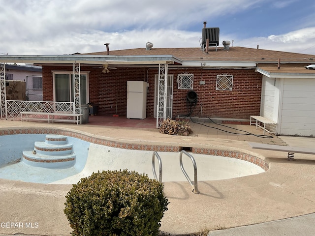 back of property with a patio area, an empty pool, and brick siding