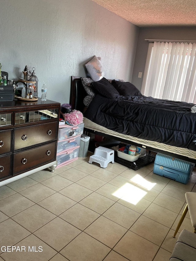 bedroom featuring a textured wall, a textured ceiling, and light tile patterned floors