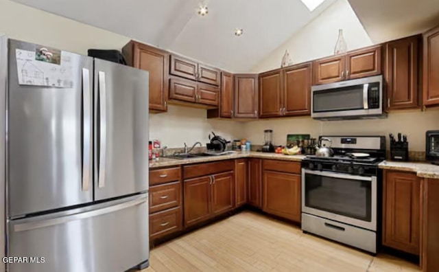 kitchen featuring light wood finished floors, light countertops, appliances with stainless steel finishes, vaulted ceiling, and a sink