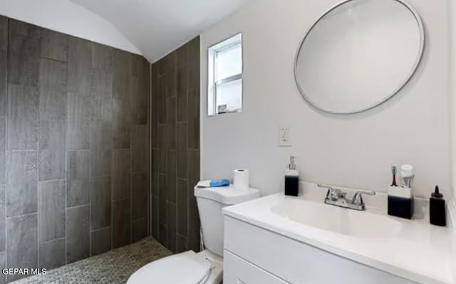 full bathroom with toilet, vaulted ceiling, a tile shower, and vanity