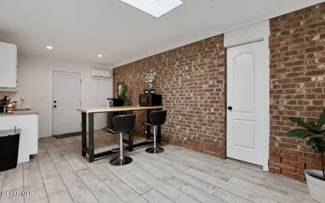 kitchen featuring white cabinetry, light wood finished floors, brick wall, and a wall mounted AC