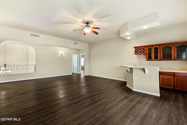 kitchen featuring arched walkways, glass insert cabinets, open floor plan, a kitchen breakfast bar, and light countertops