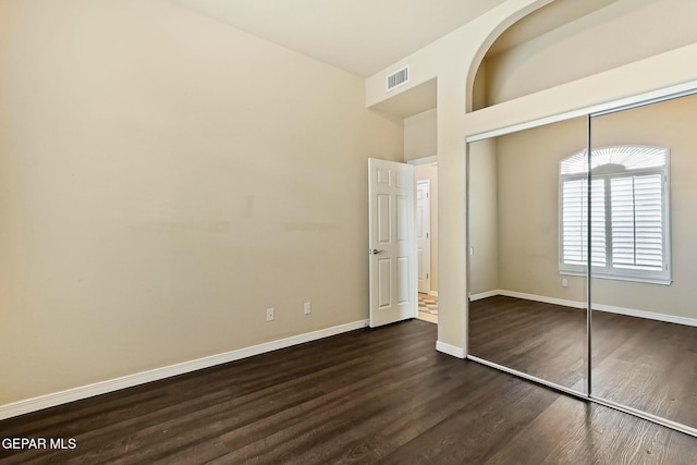 unfurnished bedroom with a high ceiling, visible vents, baseboards, a closet, and dark wood finished floors