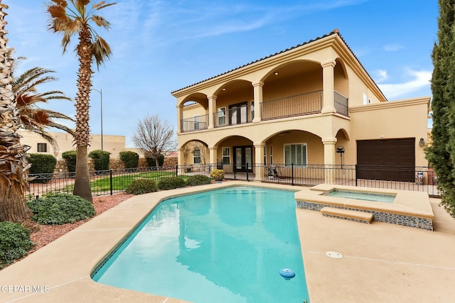 back of house featuring a pool with connected hot tub, fence, a balcony, and stucco siding