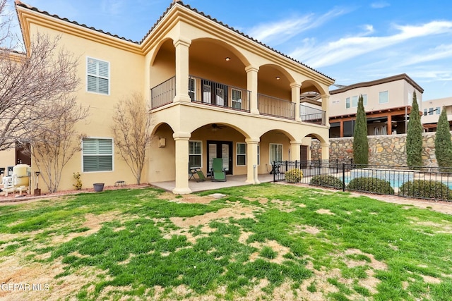 rear view of property with a lawn, a balcony, fence, a patio area, and stucco siding