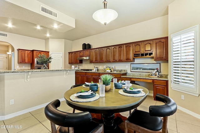 kitchen with arched walkways, under cabinet range hood, visible vents, light stone countertops, and decorative light fixtures