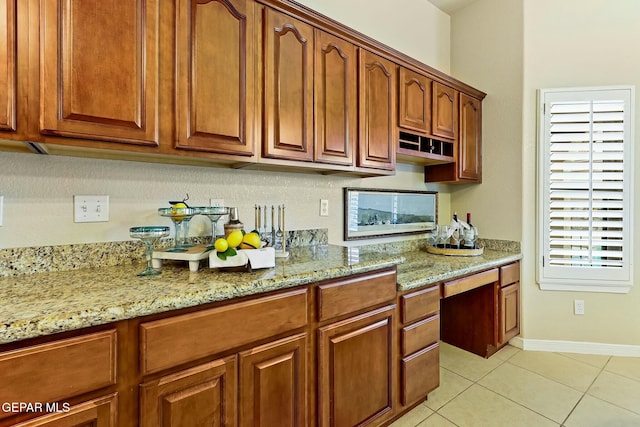 kitchen featuring light stone counters, brown cabinets, built in desk, and light tile patterned floors