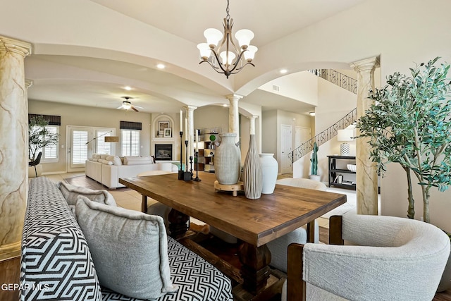 dining area featuring arched walkways, stairway, ornate columns, a fireplace, and ceiling fan with notable chandelier