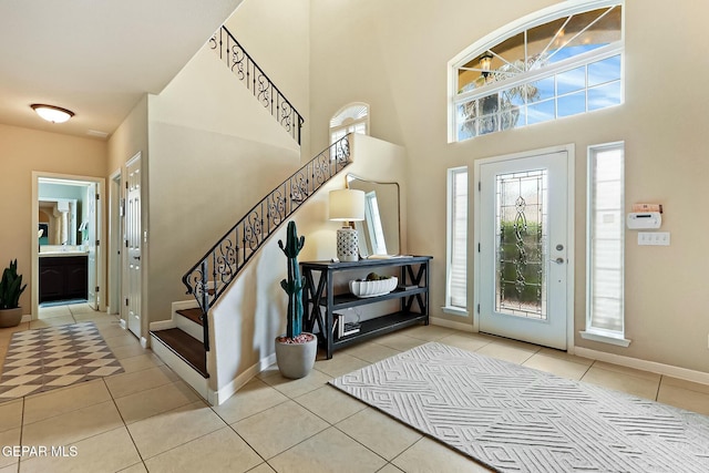 foyer featuring a towering ceiling, tile patterned flooring, stairway, and baseboards