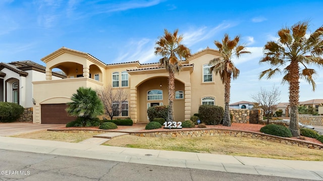 mediterranean / spanish-style house featuring a garage, driveway, a balcony, a tiled roof, and stucco siding