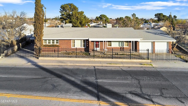 ranch-style house featuring a garage, driveway, brick siding, and a fenced front yard