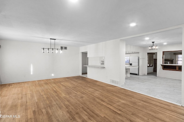 unfurnished living room with baseboards, light wood-type flooring, visible vents, and a notable chandelier