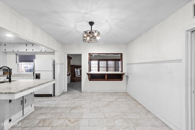 kitchen featuring light stone counters, freestanding refrigerator, hanging light fixtures, a chandelier, and a sink