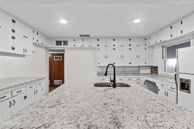 kitchen with visible vents, white cabinets, light stone countertops, white fridge with ice dispenser, and a sink