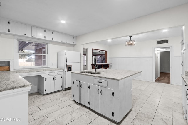 kitchen featuring a center island with sink, white cabinets, freestanding refrigerator, pendant lighting, and a sink