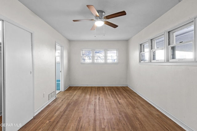 unfurnished bedroom featuring baseboards, multiple windows, visible vents, and wood finished floors