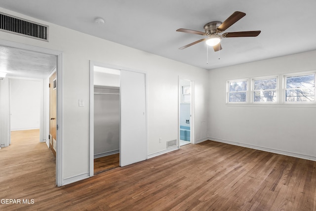 unfurnished bedroom featuring baseboards, a closet, visible vents, and wood finished floors