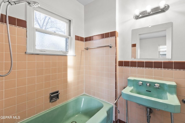 full bathroom with a wainscoted wall, a healthy amount of sunlight, a sink, and tile walls