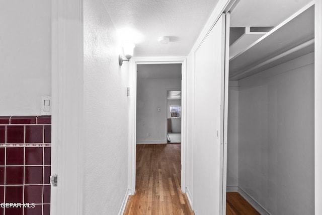 hallway with a textured ceiling, wood finished floors, and a textured wall