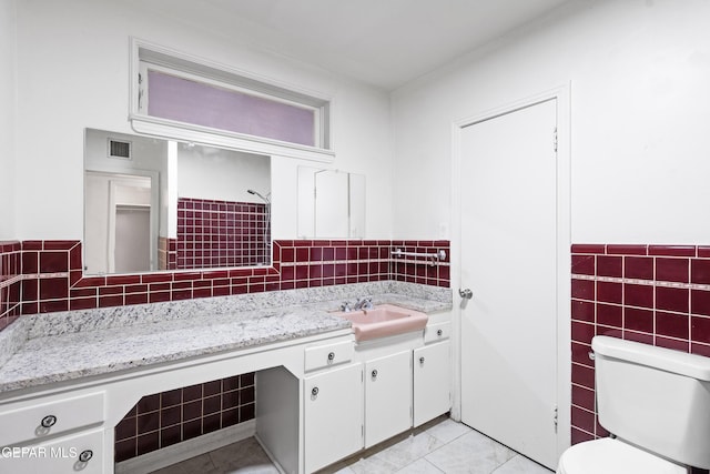 bathroom featuring visible vents, toilet, tile patterned floors, vanity, and tile walls