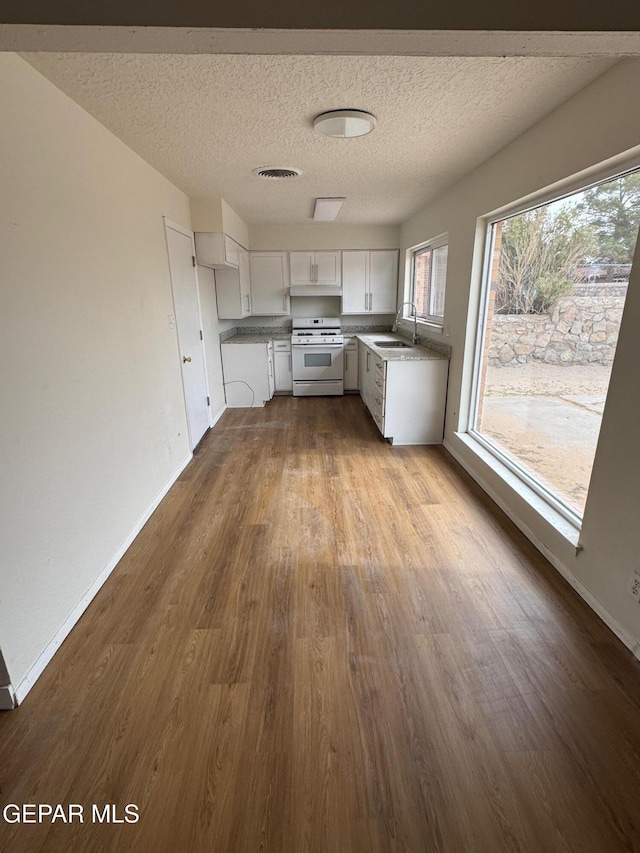 kitchen featuring visible vents, a sink, white gas stove, white cabinetry, and dark wood-style flooring