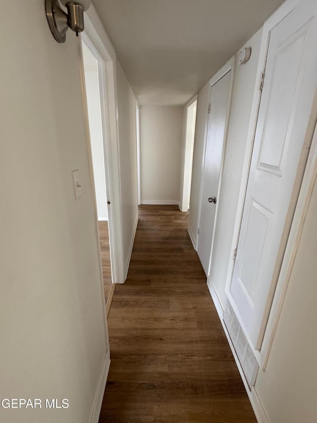 hallway with dark wood finished floors, visible vents, and baseboards