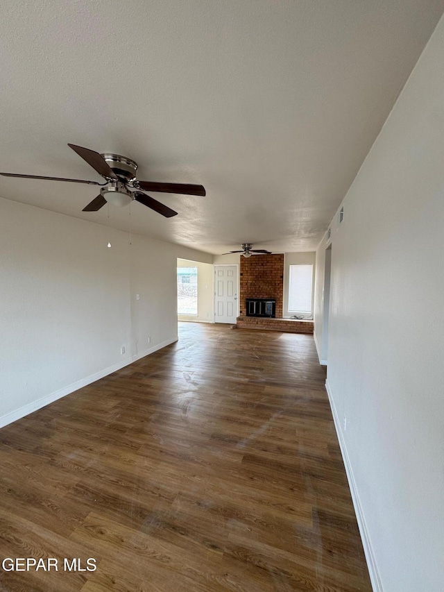 unfurnished living room with dark wood-type flooring, a brick fireplace, baseboards, and ceiling fan