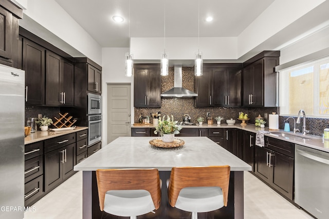 kitchen featuring wall chimney exhaust hood, stainless steel appliances, light countertops, and a center island