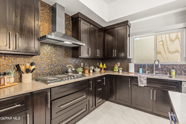 kitchen featuring a sink, light countertops, wall chimney range hood, stainless steel gas cooktop, and backsplash