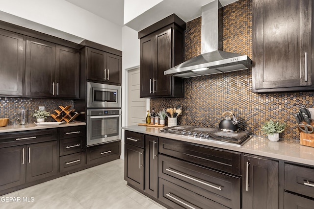 kitchen featuring light countertops, decorative backsplash, appliances with stainless steel finishes, dark brown cabinetry, and wall chimney exhaust hood