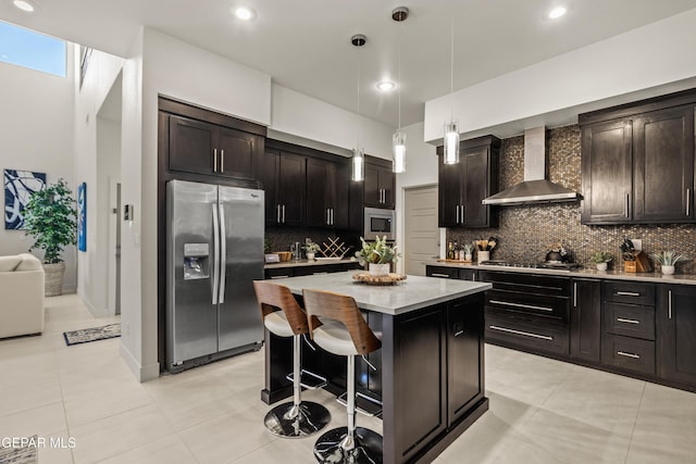 kitchen featuring stainless steel appliances, dark brown cabinets, wall chimney range hood, light countertops, and a center island