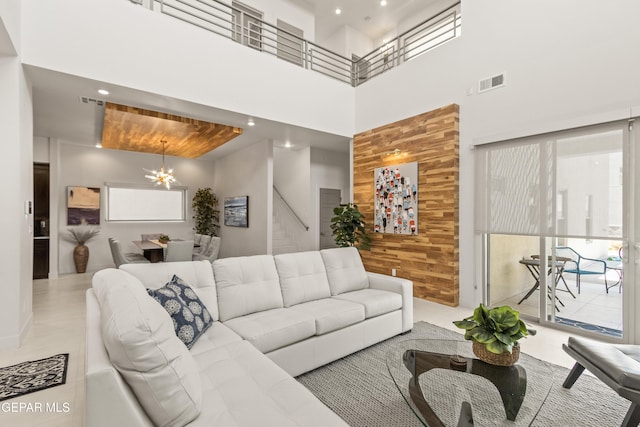 living room featuring visible vents, an inviting chandelier, stairs, a high ceiling, and wood walls